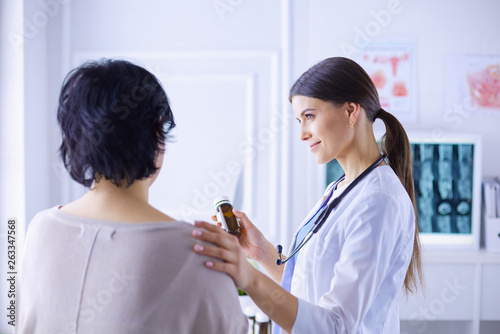 Beautiful female doctor explaining medical treatment to a patient, holding a bottle of medicaments