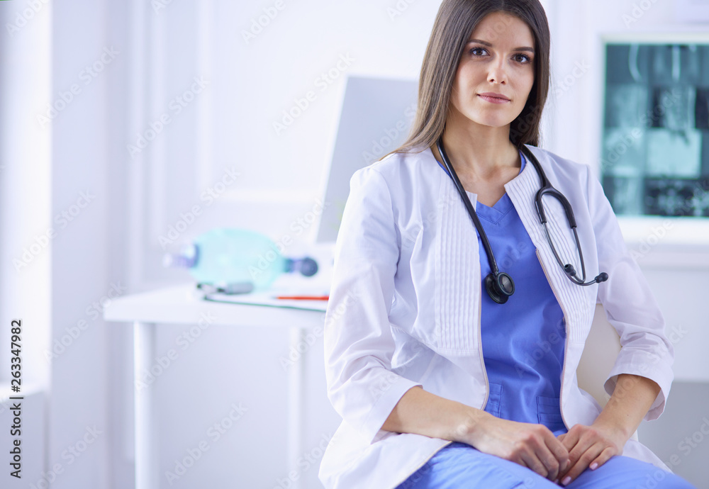 Beautiful female doctor sitting at her working place in a consulting room, smiling at the camera Beautiful female doctor sitting at her working place in a consulting room, smiling at the camera