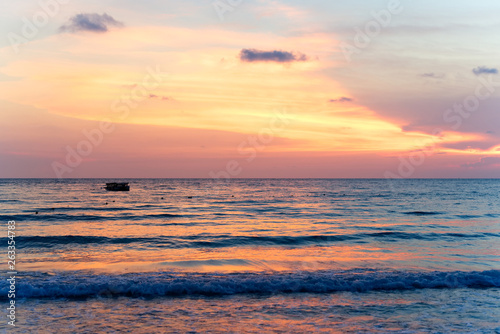 Colorful ocean beach sunset with deep orange blue sky and sun rays. Small waves coming on the beach. Travel and holiday on the beach concept. © Kawee