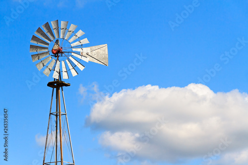 Windmill and Cloud - Antique metal windmill stands against a cloudy blue sky.