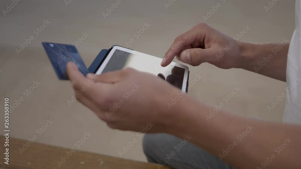 Cropped shot of man making online purchases with tablet. Male hands typing credit card number on touch screen on tablet. Online shopping concept Cropped shot of man making online purchases with tablet. Male hands typing credit card number on touch screen on tablet. Online shopping concept