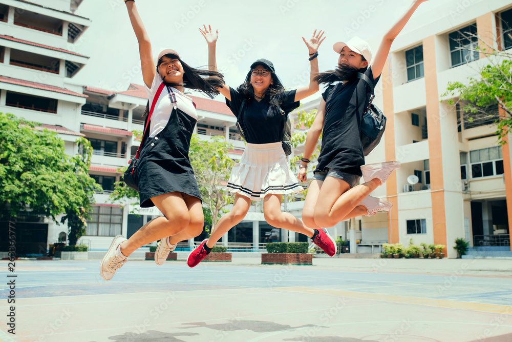 three asian teenager jumping mid air with happiness emotion against school building background