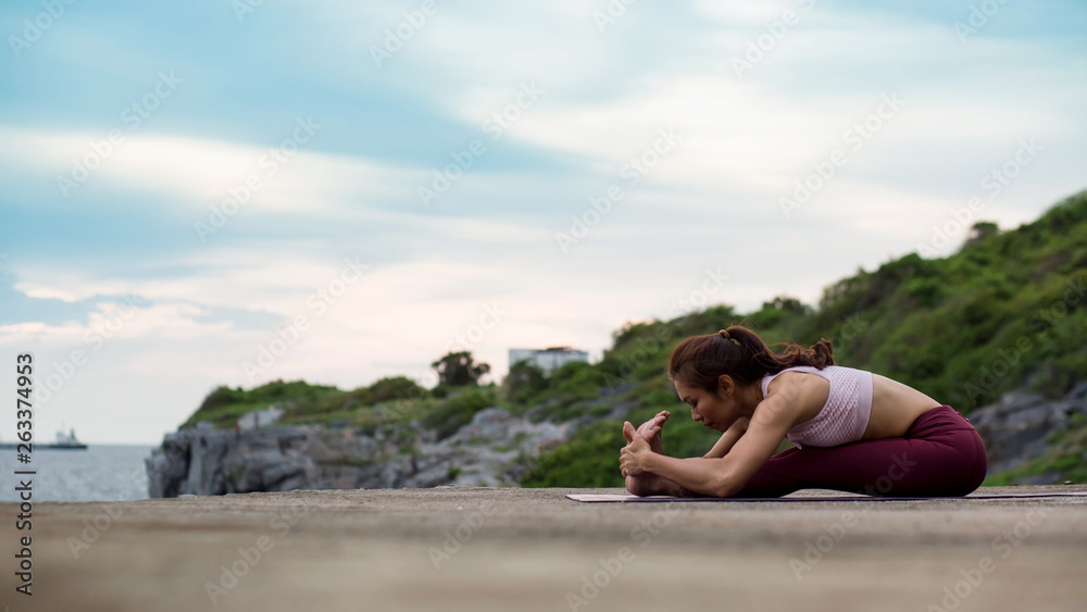 Rearview of healthy women practicing yoga. sitting in doing paschimottanasana exercise, Seated forward bend pose. hands holding foot.   .beautiful landscape view sky on evening sunlight.