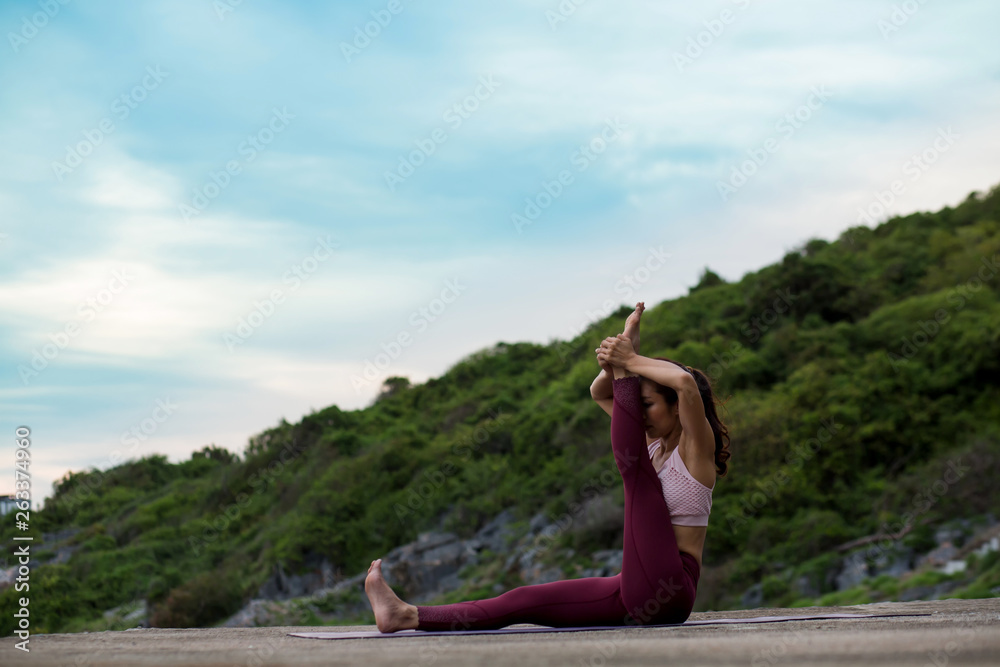 Rearview of Healthy women wearing exercise clothes yoga.  sitting in heron pose.Intense hamstring stretch with leg up and hands holding foot.   .beautiful mountain landscape view sky evening sunlight