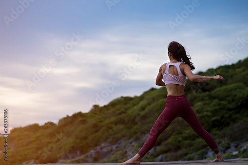 Rear view of healthy women practicing yoga. doing warm-up balance exercise standing on one the rock floor and twisting pose,   .beautiful landscape view sky on evening nature evening outdoor. © I'm Thongchai