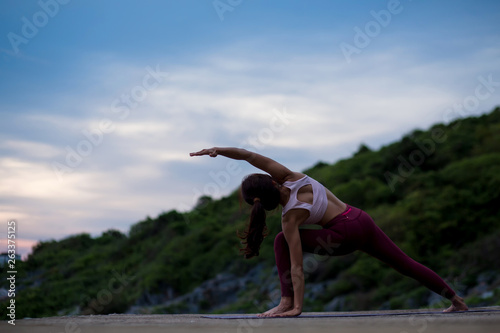 Rear view of healthy women practicing flexible yoga pose. stretching leg on mat on the rock. yoga landscape on evening view on evening nature evening outdoor, concept for exercising, health care