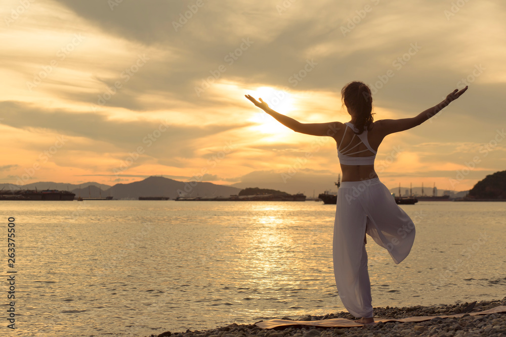 Rearview of woman practicing yoga. standing near sea. doing Tree Pose/Vrikshasana.  .beautiful landscape view sky on morning and enjoying sea view, concept for exercising, health care