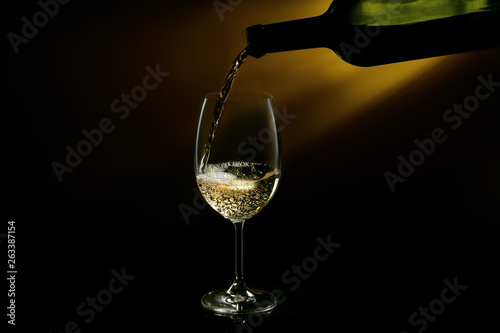 White wine pouring in a glass from a bottle. Studio shot on black background.