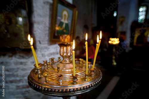 Round candlestick with burning candles in the interior of russian orthodox church. Candles under the ancient icon framed with the gold. Сelebration of holy holidays photo