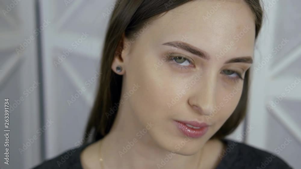 Close-up portrait of a dark-haired and green-eyed pretty girl, who made microblading eyebrows. She looks at the camera and smiles, posing. Close-up portrait of a dark-haired and green-eyed pretty girl, who made microblading eyebrows. She looks at the camera and smiles, posing.