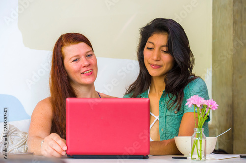 young happy and beautiful caucasian and latin women working at office cafe with laptop computer discussing as digital business partners and diversity ethnicity friends