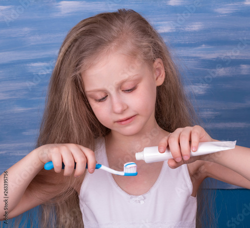 Nice little girl takes care of his teeth, squeezing toothpaste on toothbrush photo