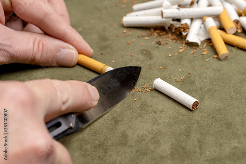 Fight against smoking. A man cuts a cigarette with a knife on the background of a pile of broken cigarettes