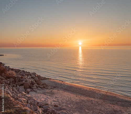 Setting sun over the ocean on a windless day. Sun reflecting in stones on the beach.