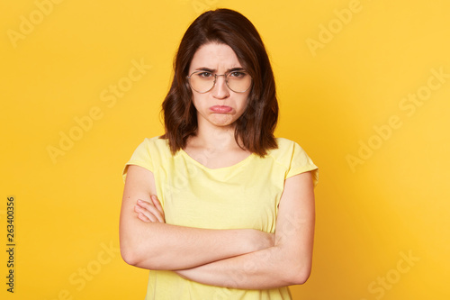Close up portrait of emotional woman with offended facial expression, has negative feelings, lady receives bad news from husband, feels disappointed, isolated over yellow background. Emotions concept