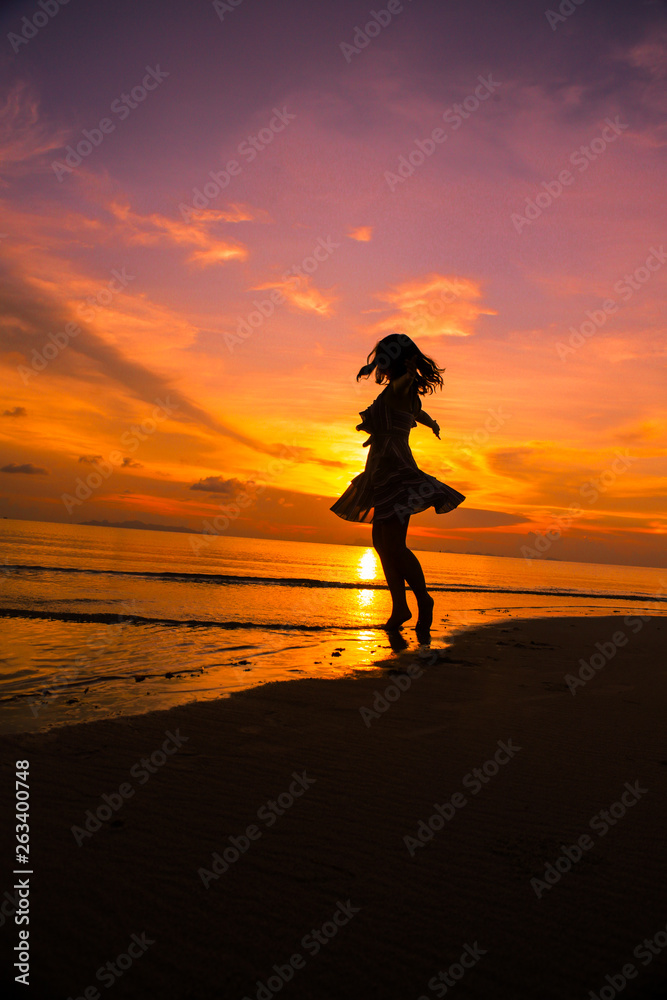 Girl jumping and dancing on the beach at sunset silhouettes 
