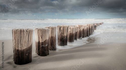 Pole heads or wave-breakers disappearing in North Sea in Holland with a blurry background of the sea and cloudy sky