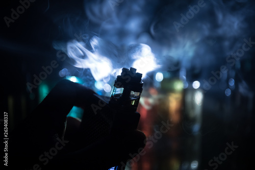 Vape concept. Electronic Cigarette vape explosion. Smoke clouds and vape liquid bottles on dark background. Light effects. Useful as vape advertisement.