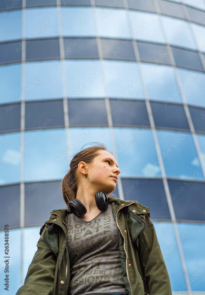 Outdoor portrait of young teenager brunette girl with long hair. Glass building on background with copy space