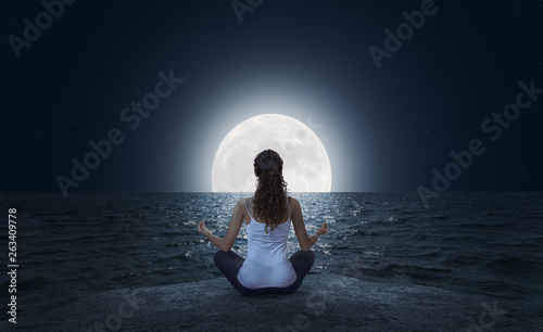 Young woman meditating on the beach at full moon