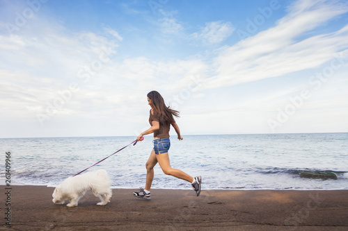 Young woman playing with her dog on the sea beach at sunny day