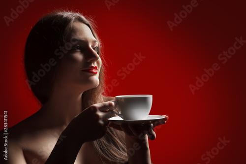 Attractive lady brunette with pleasure holding a empty cup in hand in studio at the red background