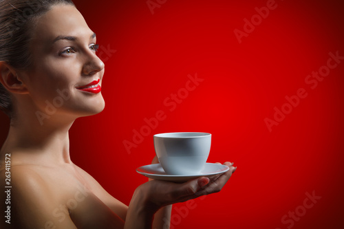 Attractive lady brunette with pleasure holding a empty cup in hand in studio at the red background