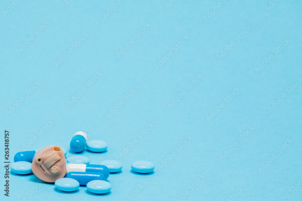 Hearing aid and blue pills on blue background. Medical, pharmacy and healthcare concept. Copy space. Empty place for text or logo