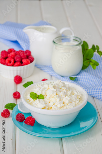 Homemade fresh cottage cheese in a bowl with raspberry berries, sour cream, honey and mint leaves.