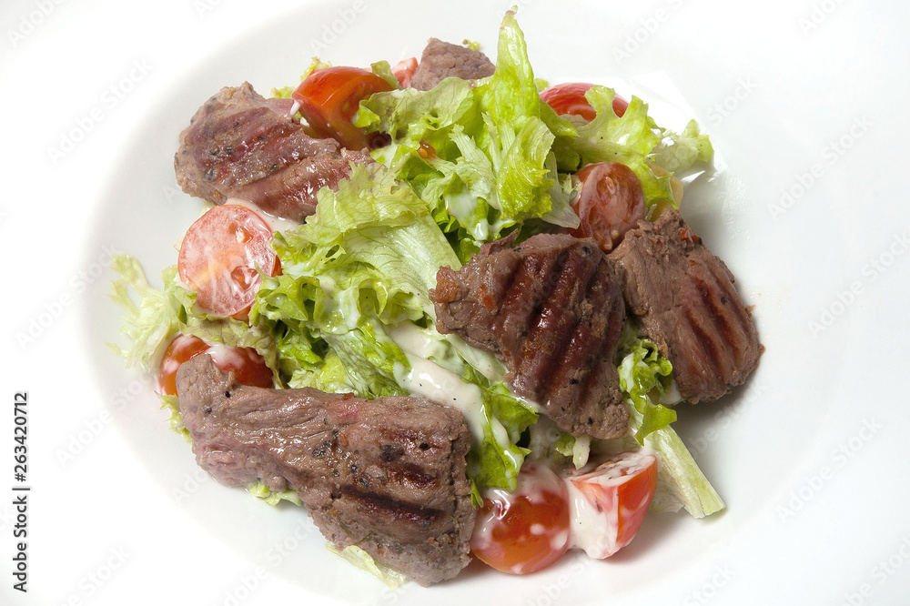 Veal salad, salad with large slices of veal and fresh vegetables on a plate on a black background.