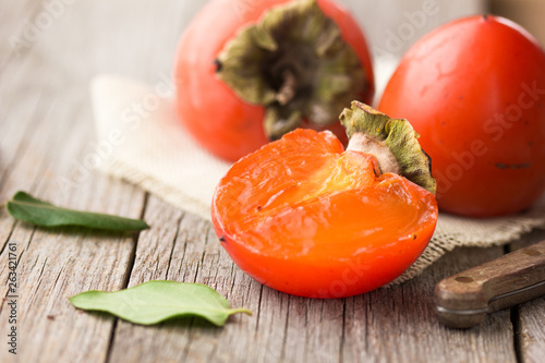 Persimmon cut fruits in basket and persimmon colored leaves on wooden background