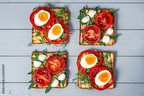 Sandwiches with fresh vegetables avocado with arugula and boiled eggs on fried toast with mozzarella cheese on a gray wooden background with a place for copy space, flat lay