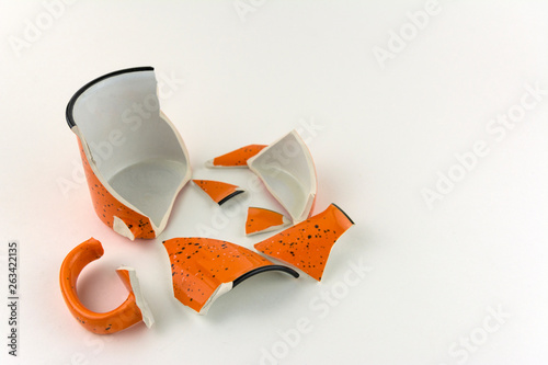 Broken orange mug on white background. Numerous pieces of the Cup