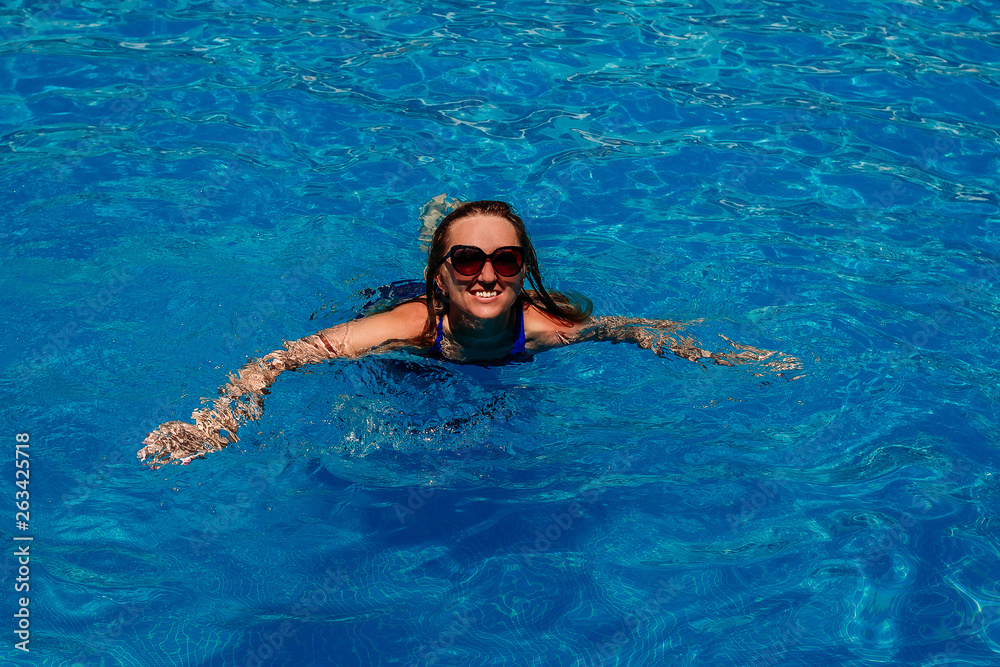 a young woman in sunglasses swims in the pool