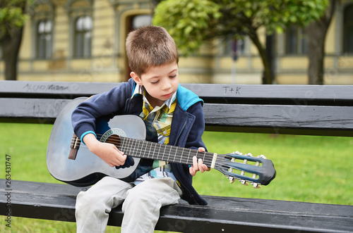 child boy playing on guitar in a park