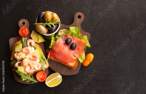 Open sandwiches with salmon, shrimp, arugula and olives on rye bread, top view with copy space
