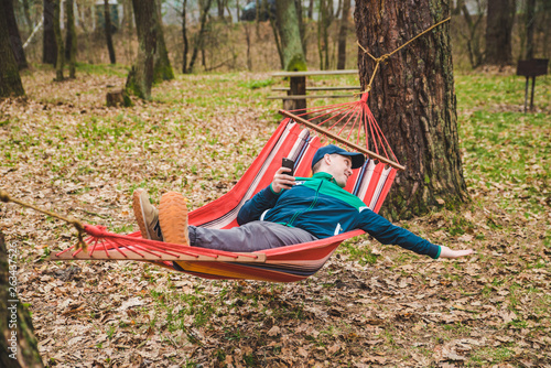 young man laying in hammock surfing in phone