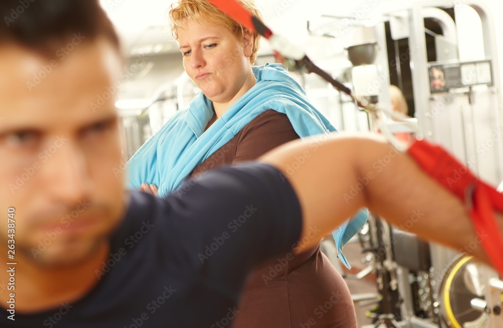 Obraz premium Fat woman watching athletic man in gym
