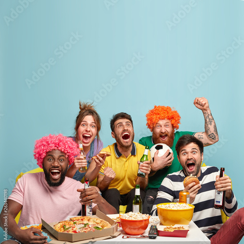 Foto Photo of friends watch soccer game, celebrate goal, clench fists, enjoy watching sport competition, have delicious snack, drink cold beer, spend spare time at home