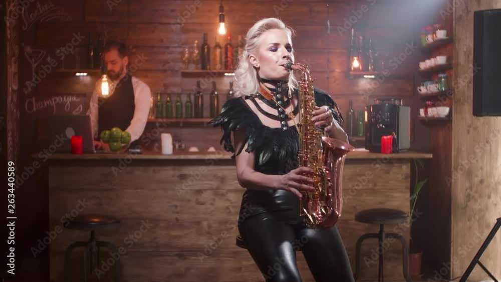 Pretty woman in sexy black leather clothes plays a song on a saxophone. Female musician sings a jazz song at a golden sax.