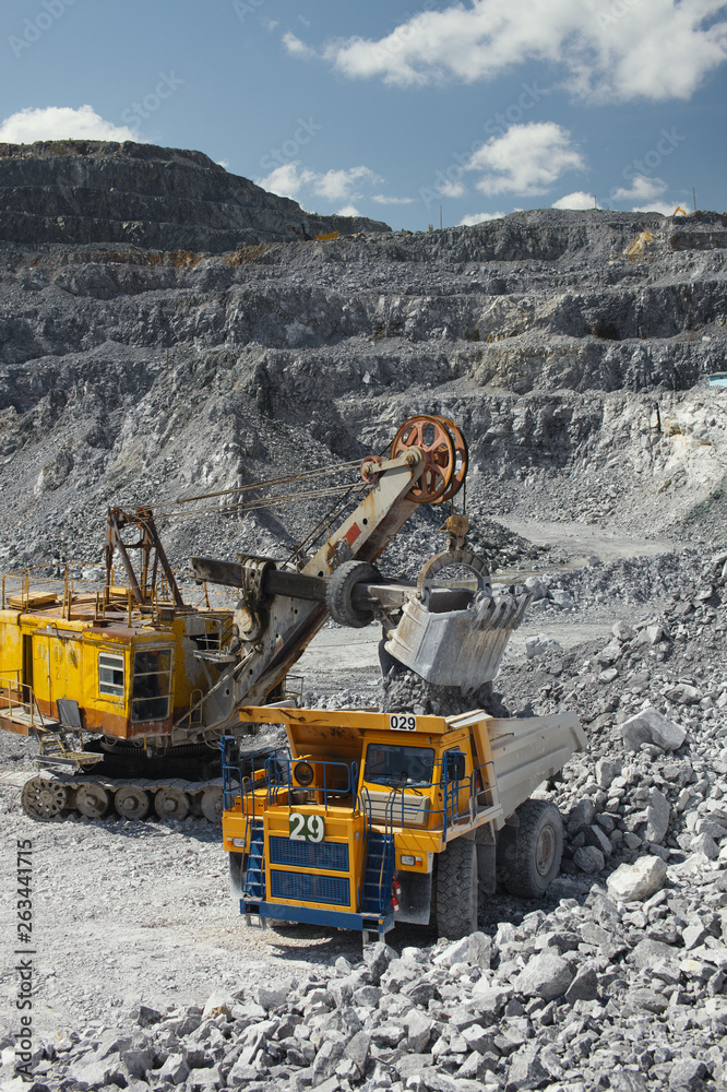 Heavy mining excavator loads rock ore into a dump-body large mining truck. Quarry equipment. Mining industry.