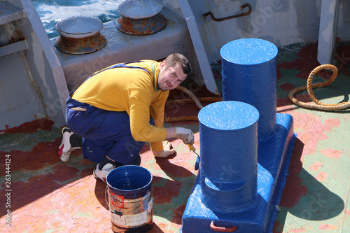 Seaman paints a bollard and deck mechanisms on the deck of a ship photo