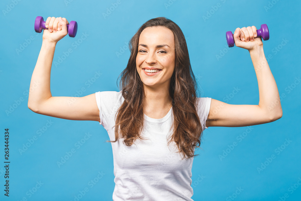Healthy lifestyle! Side view portrait of a pretty young sportswoman doing exercises with dumbbells isolated on a blue background. Healthy lifestyle! Side view portrait of a pretty young sportswoman doing exercises with dumbbells isolated on a blue background.