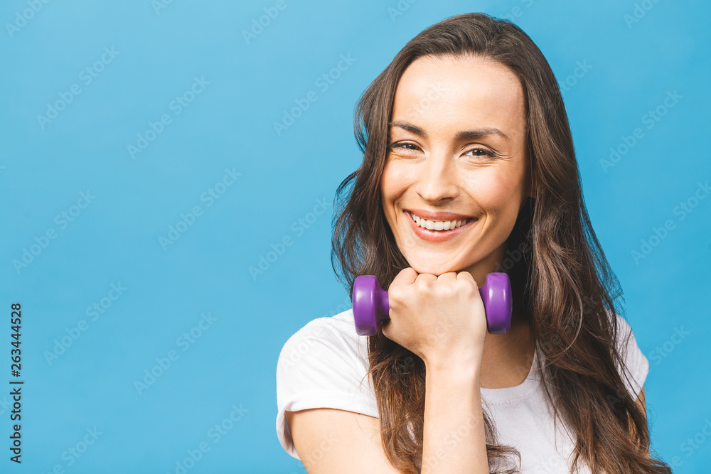 Healthy lifestyle! Side view portrait of a pretty young sportswoman doing exercises with dumbbells isolated on a blue background. Healthy lifestyle! Side view portrait of a pretty young sportswoman doing exercises with dumbbells isolated on a blue background.