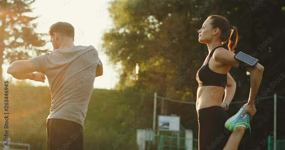 Happy sporty Caucasian guy and girl doing sport exercises and workout on the stadium on a sunny summer day.