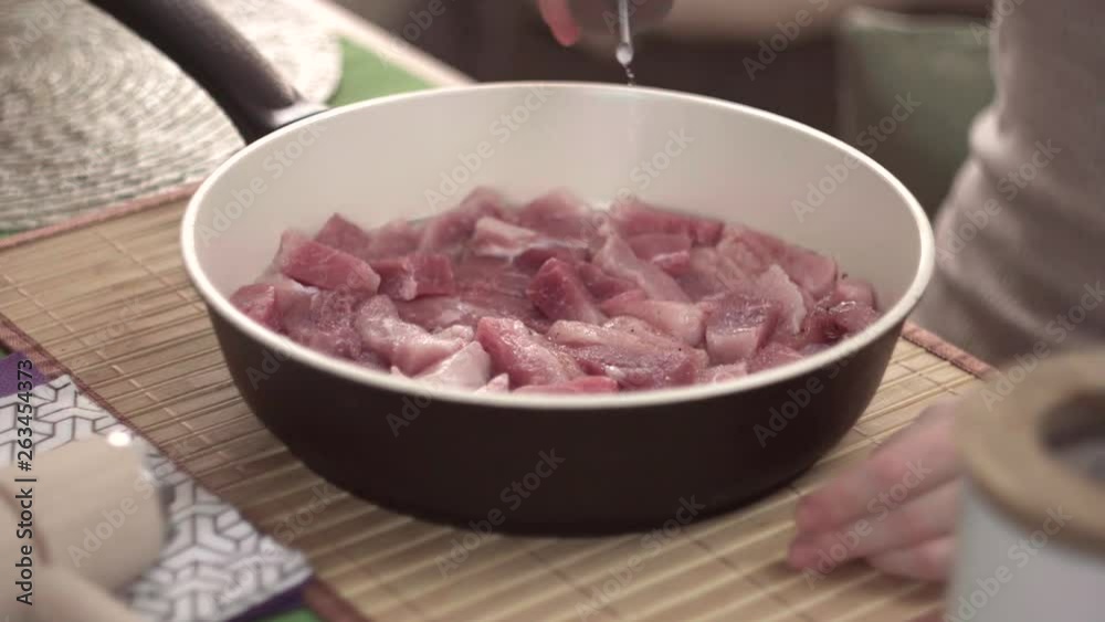 Girl sprinkles salt and pepper meat in a frying pan, close-up Girl sprinkles salt and pepper meat in a frying pan, close-up