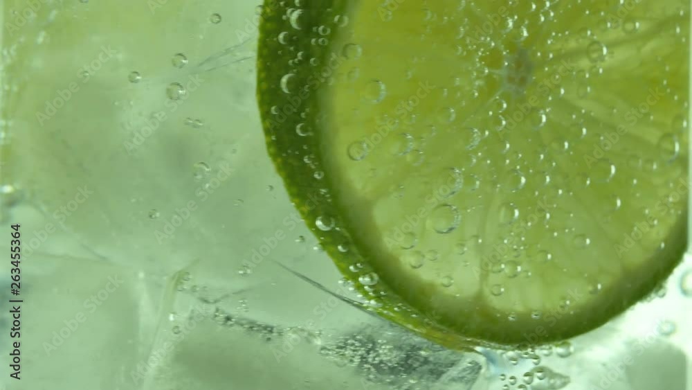 Glass of sparkling water soda drink with ice and lime lemon slice rotating.
