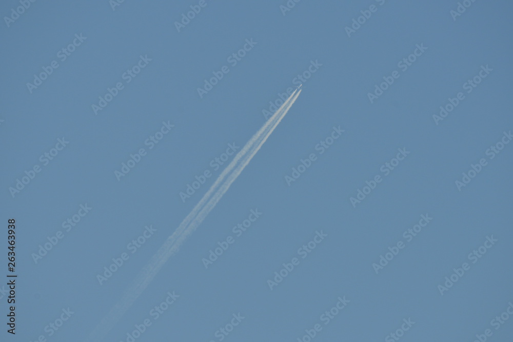 Commercial aircraft at very high altitude with white contrail on cloudless blue sky