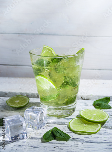 Mojito cocktail with slices of lime and mint leaves in highball glass on a wood table. White background.