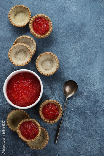 Tartlets filled with red caviar, flatlay on a blue stone background, vertical shot with copy space
